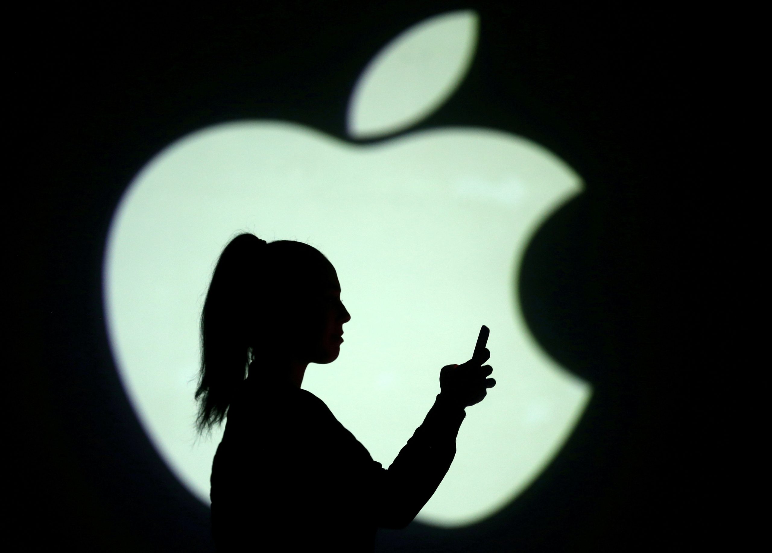 FILE PHOTO: Picture illustration of a silhouette of a mobile user next to a screen projection of the Apple logo